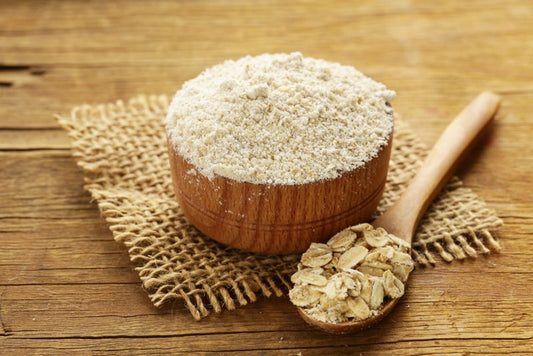 A bowl of oat flour with a spoon of rolled oats besides it