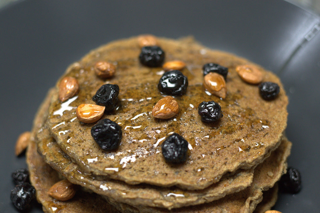 A plate of raw banana flour pancakes topped with sweet apricots, dried blueberries and honey