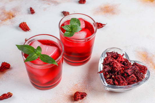 2 Glasses of hibiscus iced tea with mint and a bowl of dried hibscus flowers besides it